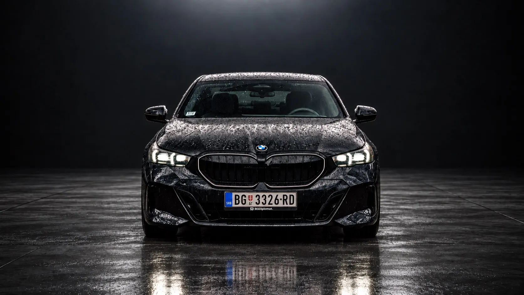 A black BMW 5 Series with its headlights on, on a wet studio floor