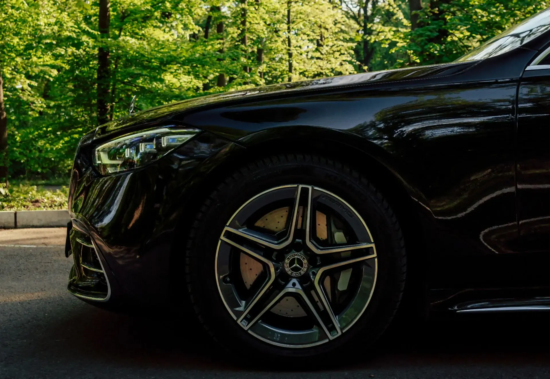 The front wheel of a black Mercedes-Benz S-Class against green trees