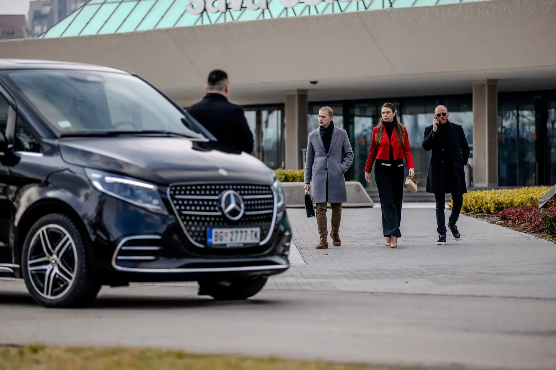 A chauffeur beside a black Mercedes-Benz V-Class as three travellers walk towards him