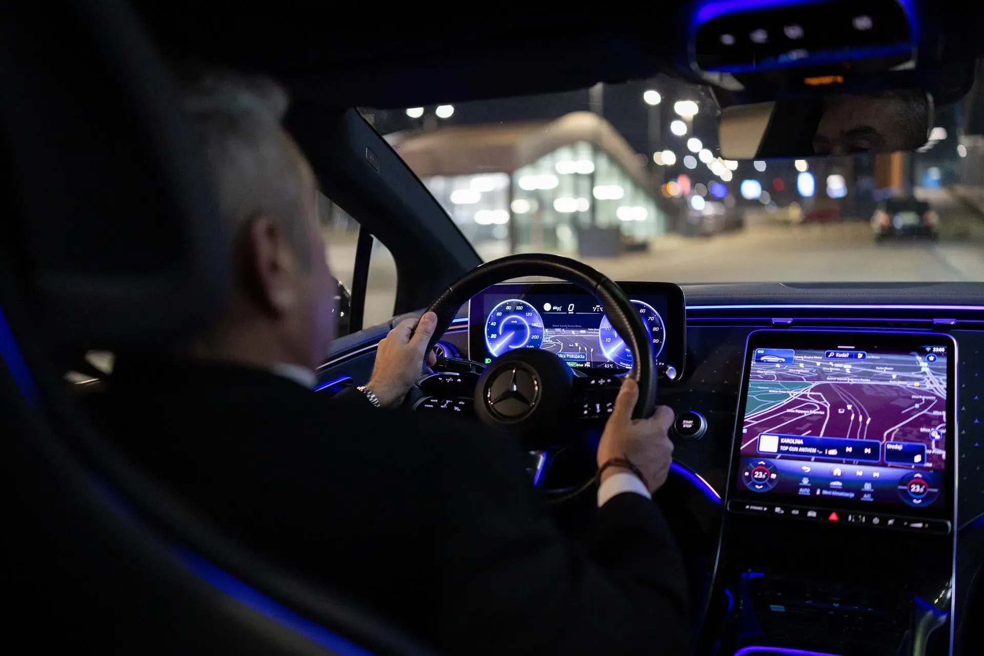 A chauffeur at the wheel of a Mercedes at night, city lights ahead