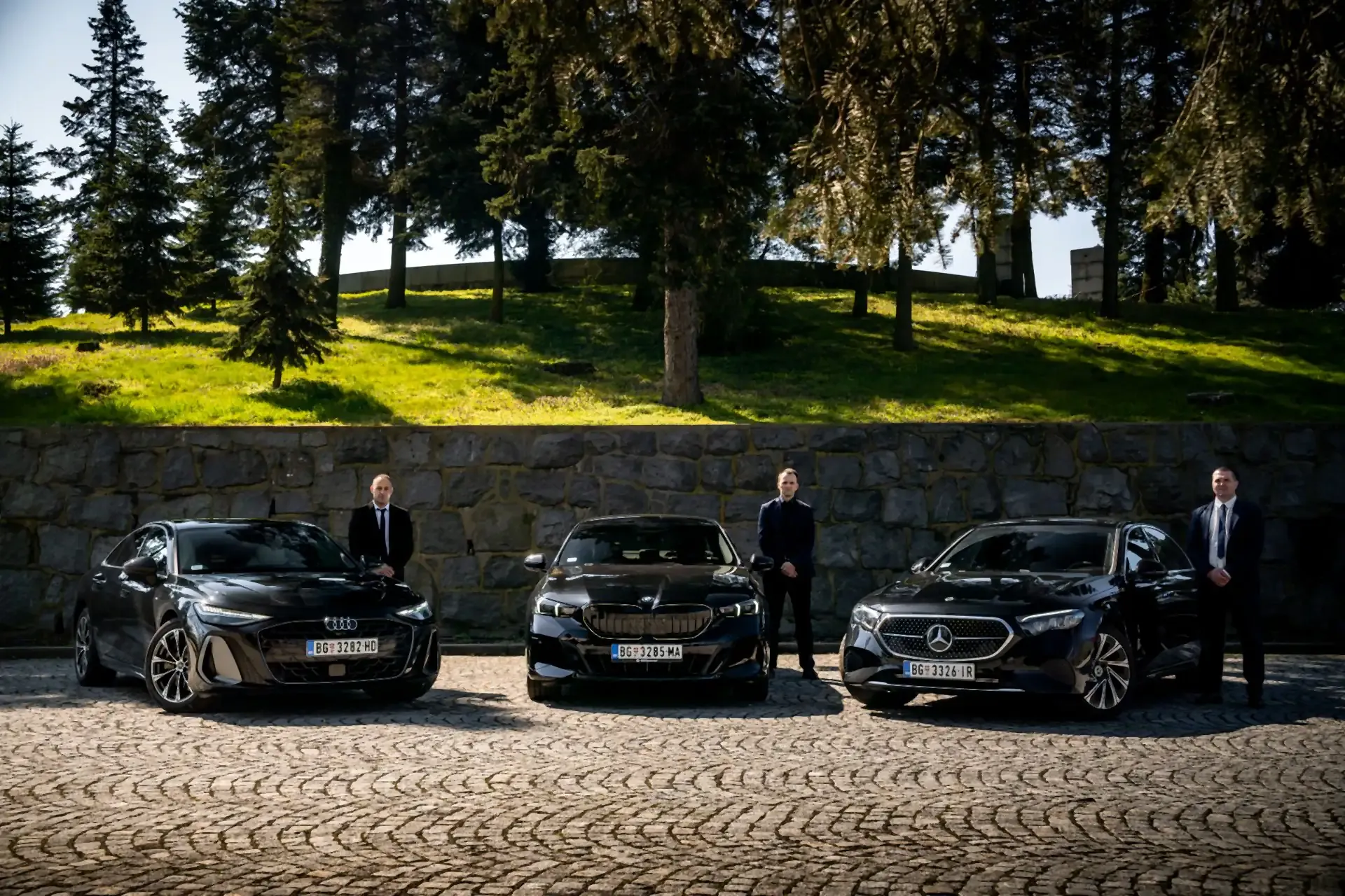 Three BG Diplomat chauffeurs beside a black Audi, BMW and Mercedes-Benz