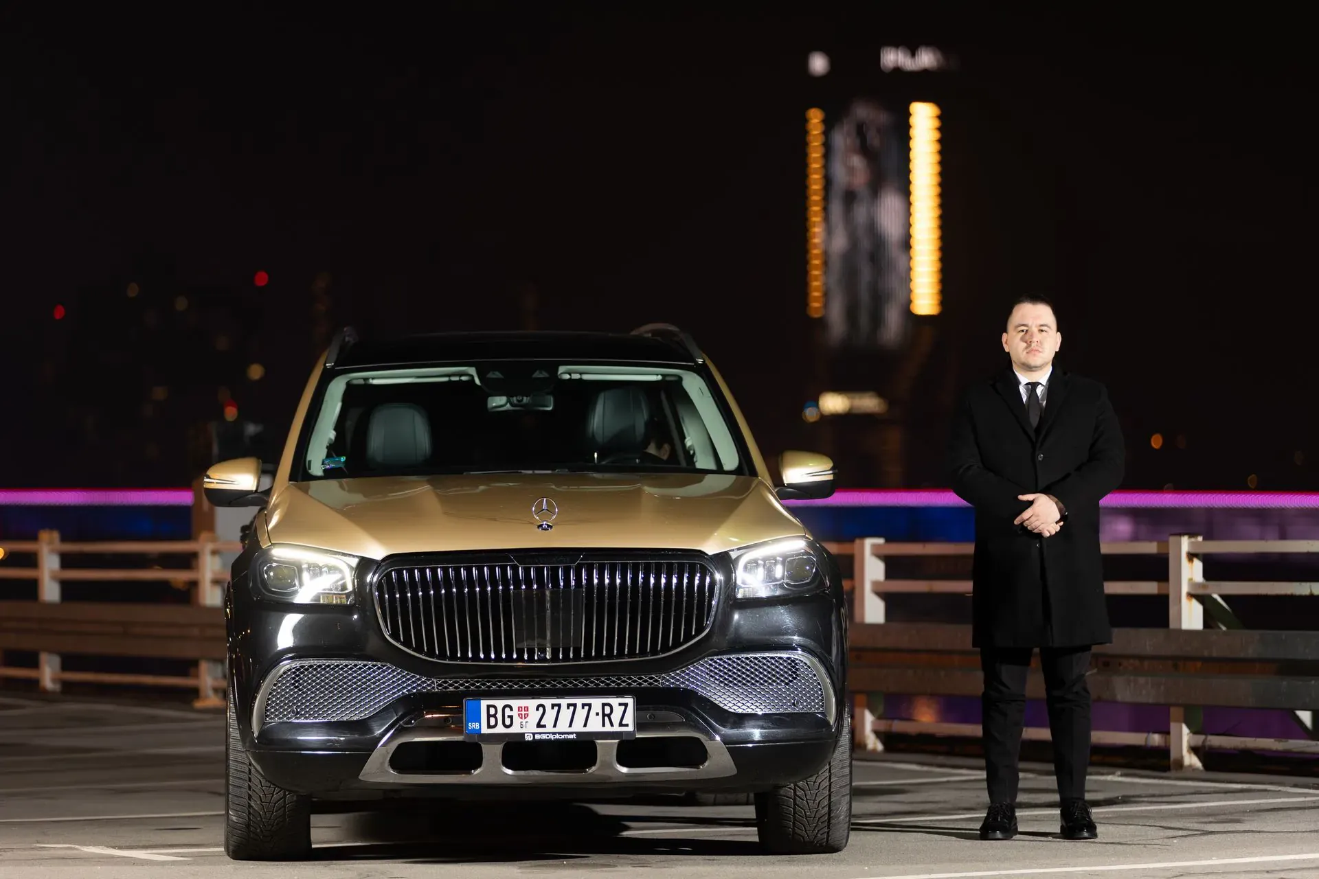 A chauffeur in a dark coat beside a Mercedes-Maybach GLS at night